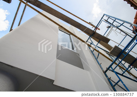 Low angle detail of house renovation and construction project with scaffolding. new exterior paint and window installation show hopeful progress of home improvement 130884737