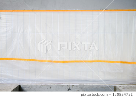 Protective plastic sheet covering wall during house renovation. Careful construction detail shows preparation work protecting tile from dust and damage in messy site Protective plastic sheet covering wall during house renovation. Careful construction detail shows preparation work protecting tile from dust and damage in messy site 130884751