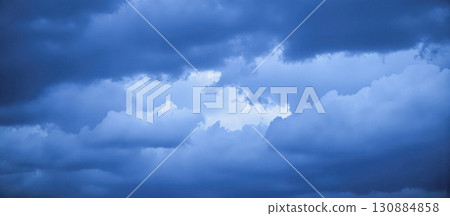 Dramatic blue storm clouds clearing to reveal patch of bright sky, weather background representing powerful change and amazing breakthrough Dramatic blue storm clouds clearing to reveal patch of bright sky, weather background representing powerful change and amazing breakthrough 130884858