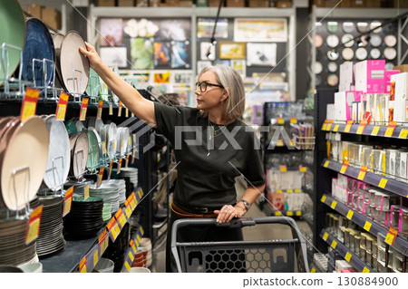 Shoppers explore home goods aisle while selecting plates in a retail store during daytime 130884900
