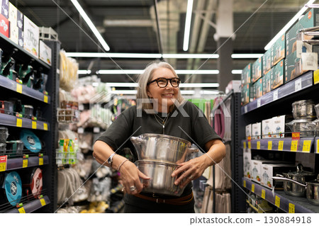 Happy woman shopping for kitchenware in a well-stocked store aisle during daylight hours 130884918