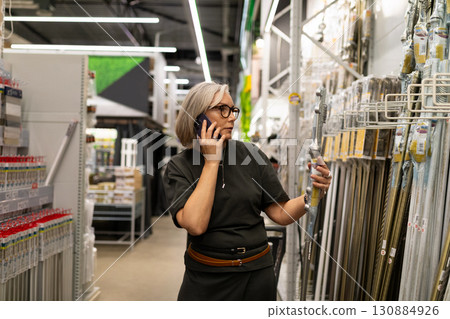 Woman shopping for tools and talking on the phone in a hardware store during the day 130884926