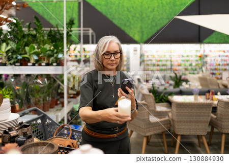 Woman shopping for home decor items while checking her phone in a vibrant store interior filled with Woman shopping for home decor items while checking her phone in a vibrant store interior filled with 130884930