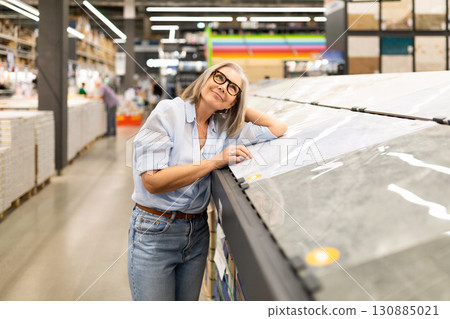 Woman exploring tile options in a home improvement store during daylight hours in a busy shopping Woman exploring tile options in a home improvement store during daylight hours in a busy shopping 130885021