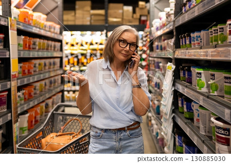 Woman shopping in a grocery store aisle while talking on the phone during afternoon hours 130885030