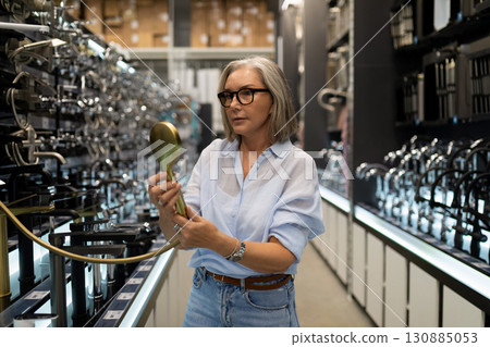 Woman exploring modern kitchen fixtures in a showroom, engaging with a stylish faucet in a 130885053
