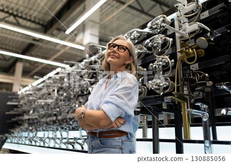 Smiling woman in blue shirt admires innovative designs at a modern kitchenware expo in a bright 130885056