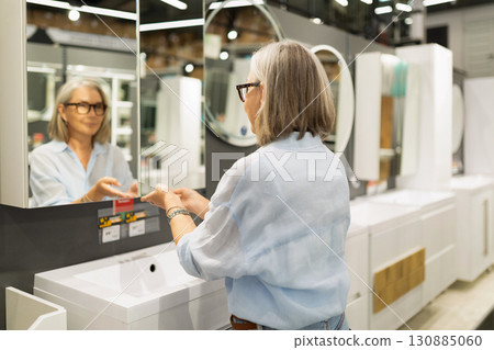 Woman examines bathroom fixtures in modern home improvement store during daytime shopping 130885060