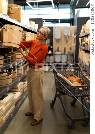Senior woman explores home goods aisle while shopping for storage baskets in a modern retail store Senior woman explores home goods aisle while shopping for storage baskets in a modern retail store 130885067