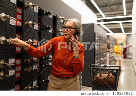 Woman shopping for home improvement materials while talking on her phone in a retail store aisle 130885081