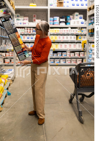 Older woman selects paint color swatches in a home improvement store aisle during the day in a well 130885091