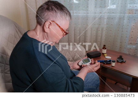 an older adult woman utilizing a handheld glucometer to test her blood sugar levels from the comfort of her own home 130885473