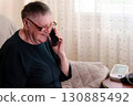 An elderly person utilizes a smartphone while a health monitoring apparatus is placed alongside them, highlighting the embrace of modern conveniences among the older generation 130885492