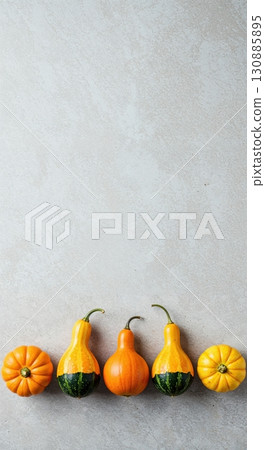 A minimalist flat lay of five small, colorful gourds and mini-pumpkins arranged in a neat row on a light textured background, featuring ample copy space above. 130885895