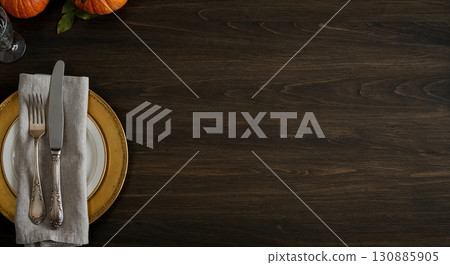 An elegant gold and white dinner plate with a linen napkin, silver fork, and knife is meticulously arranged on a dark wooden table, accompanied by small orange pumpkins and a green leaf, creating a. An elegant gold and white dinner plate with a linen napkin, silver fork, and knife is meticulously arranged on a dark wooden table, accompanied by small orange pumpkins and a green leaf, creating a. 130885905