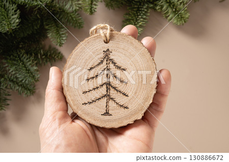 Christmas toy made of decorative wooden slice with ornament as Xmas tree on beige background. Handmade hobby. DIY. Nature material. Xmas decoration. Eco friendly. Zero waste. Sustainable gifts. View 130886672
