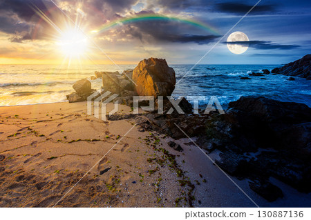 landscape by the sea in summer. day and night time change concept. beautiful beach with rocks washed by calm waves with sun and moon at twilight. view to horizon under blue sky with clouds 130887136