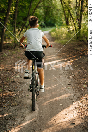 Teenager riding bicycle along forest trail on sunny day. Outdoor activity, adventure and healthy lifestyle concept 130887419