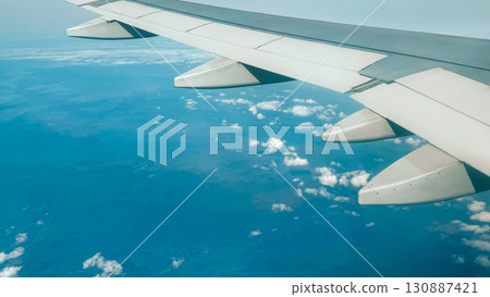 Gazing from a plane's window, the view unfolds with a tranquil blue ocean below, dotted with clouds casting shadows upon the water's surface, embodying the serene freedom of flying Gazing from a plane's window, the view unfolds with a tranquil blue ocean below, dotted with clouds casting shadows upon the water's surface, embodying the serene freedom of flying 130887421