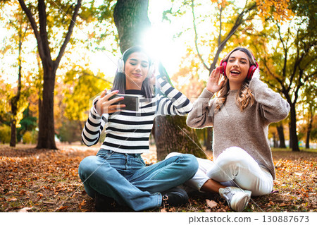 Friends enjoying autumn vibes while listening to music in the park during sunset 130887673