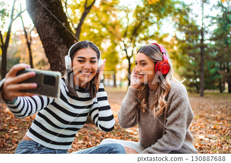 Girls enjoying music and laughter in a colorful autumn park together Girls enjoying music and laughter in a colorful autumn park together 130887688