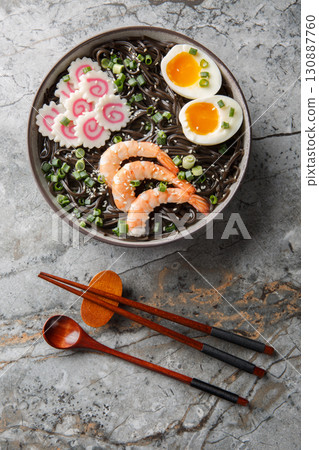 Soba buckwheat noodles with shrimp, kamaboko, green onion and egg close-up in a bowl. Vertical top view 130887760