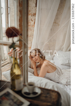 a young blonde woman in a white dress on white sheets by the window a young blonde woman in a white dress on white sheets by the window 130887962