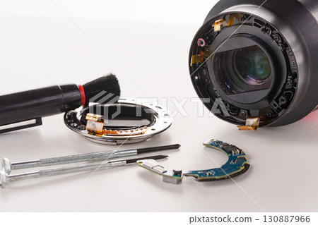 A broken lens of a professional camera and repair tools on a white table. A broken lens of a professional camera and repair tools on a white table. 130887966