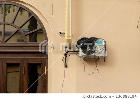 An air conditioner with large coil of wires for connection is installed on facade of the house. An air conditioner with large coil of wires for connection is installed on facade of the house. 130888194