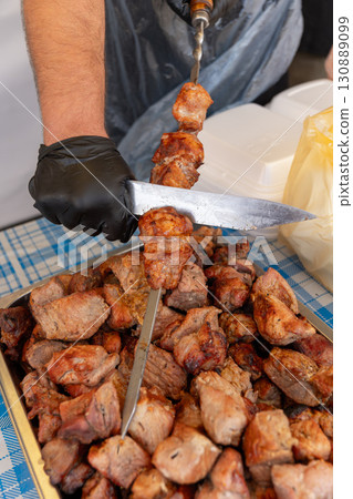 Strong male hands in black rubber gloves removing freshly grilled shish kebab from skewer Strong male hands in black rubber gloves removing freshly grilled shish kebab from skewer 130889099