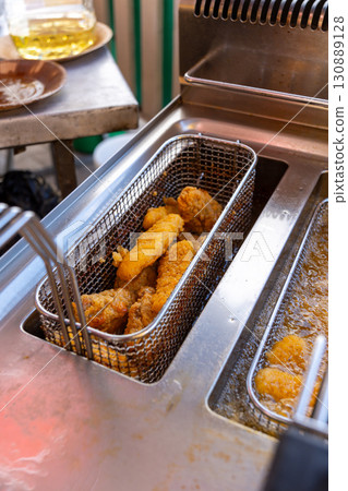 Close-up of deep fryer baskets with sizzling chicken nuggets, onion rings and french fries 130889128