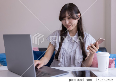 A Japanese woman working on a PC with a smartphone in her hand in the living room 130889606