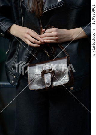 A stylish model in a black leather jacket showcases a unique black leather cross-body bag with a glossy sheen and a front flap pocket A stylish model in a black leather jacket showcases a unique black leather cross-body bag with a glossy sheen and a front flap pocket 130889901