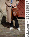 A stylish female model in a classic beige coat and sneakers showcases a sophisticated brown leather backpack with a unique flap closure and buckle detail 130889917