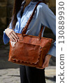 A professional close-up shot of a model showcasing a refined brown leather tote bag with unique braided handles and a decorative front pocket 130889930