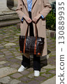 A stylish urban shot captures a woman in a beige coat and sneakers, showcasing a spacious leather tote bag with contrasting handles 130889935