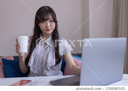 A Japanese woman working on a PC in the living room with a mug in her hand 130890103