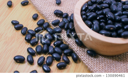 Close-up of black beans in a wooden bowl with beans scattered on burlap sack and wooden background. Perfect for concepts of organic farming 130890461