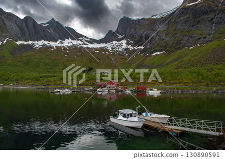 Calm Fjord With Boats And Red Huts In Front Of Snowy Mountains On Senja Island In Norway Calm Fjord With Boats And Red Huts In Front Of Snowy Mountains On Senja Island In Norway 130890591