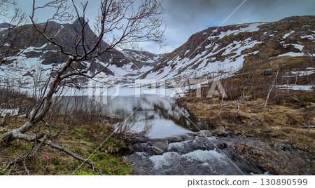 Frozen Lake And Wild River With Waterfall From Snowy Mountains On Senja Island In Norway 130890599