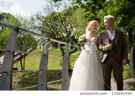 Newlyweds enjoying a serene moment on a bridge surrounded by nature 130891499