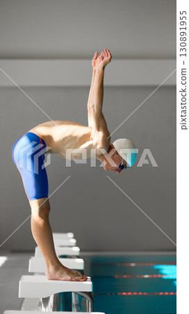 Professional swimmer on starting block preparing for dive in competition 130891955