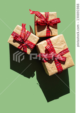 Three craft paper gift box with red plaid ribbon on green background. 130891988