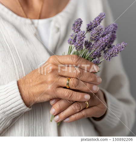 Woman holding lavender bouquet with gold rings against gray background 130892206