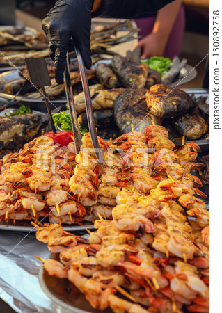 Grilled Shrimp Skewers. Description: Skewers of grilled shrimp being served with tongs at seafood stall. Concept of grilled seafood, barbecue, outdoor food festival Grilled Shrimp Skewers. Description: Skewers of grilled shrimp being served with tongs at seafood stall. Concept of grilled seafood, barbecue, outdoor food festival 130892758