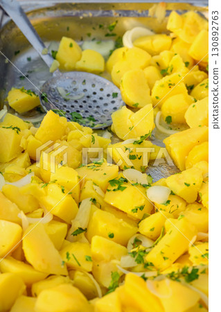 Freshly cooked yellow potatoes with chopped parsley and onion slices in a tray. Concept of boiled potatoes, vegetarian meal, and simple homemade food Freshly cooked yellow potatoes with chopped parsley and onion slices in a tray. Concept of boiled potatoes, vegetarian meal, and simple homemade food 130892763
