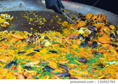 Traditional Spanish paella with rice, shrimp, mussels, and clams cooked in a large pan. Concept of seafood paella, Mediterranean cuisine, festive food tradition Traditional Spanish paella with rice, shrimp, mussels, and clams cooked in a large pan. Concept of seafood paella, Mediterranean cuisine, festive food tradition 130892764