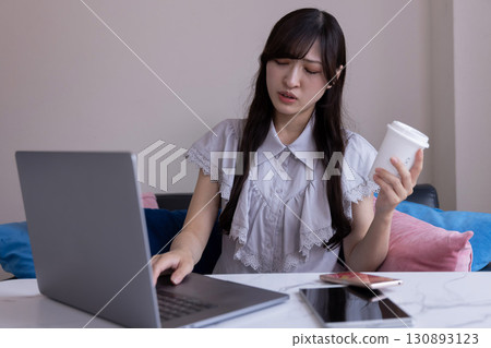 A Japanese woman working on a PC in the living room with a worried expression 130893123