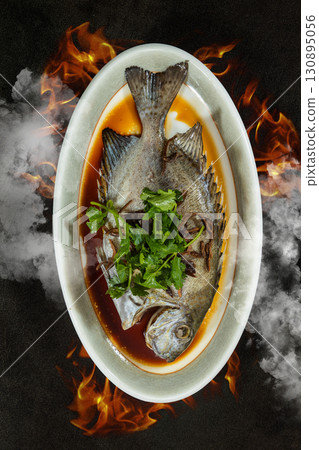 a Chinese seafood dish, steamed fish with dried citrus peel. set against a dramatic backdrop of rising steam and flickering flames a Chinese seafood dish, steamed fish with dried citrus peel. set against a dramatic backdrop of rising steam and flickering flames 130895056