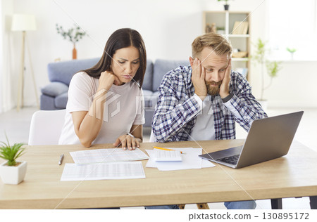 Sad focused young couple calculating bills in worry, discussing planning budget together, serious Sad focused young couple calculating bills in worry, discussing planning budget together, serious 130895172
